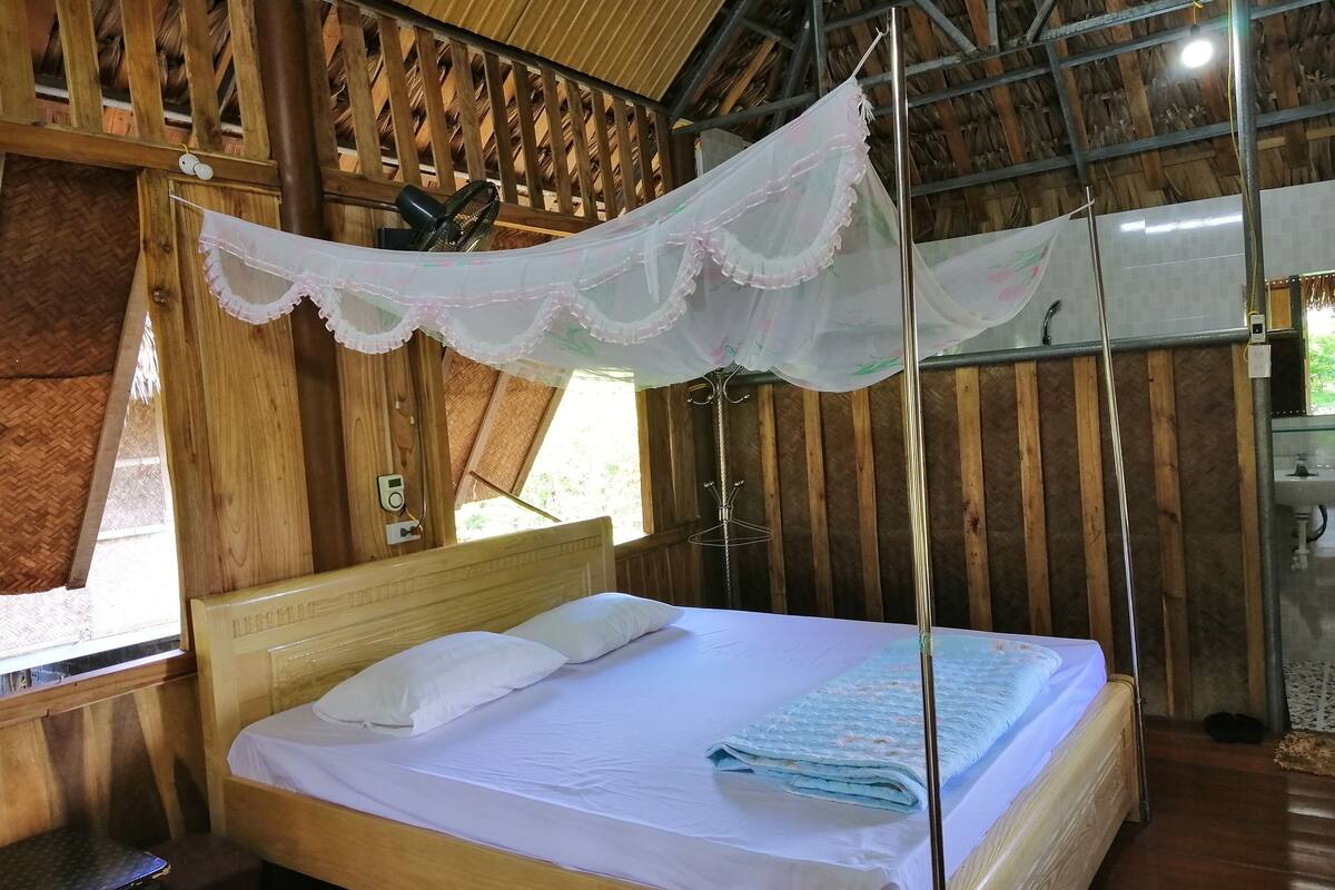 Ein Zimmer mit Holzboden, einem Bett, einem Moskitonetz und einem Fenster.