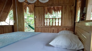 Een houten kamer met een bed, een hangmat en een raam met uitzicht op groen.