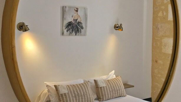 A bedroom with a large mirror, a bed with white linens, striped pillows, a wall-mounted painting, and two wall sconces. - Notre Dame Chauvigny - Chambres d'hôtes (Chauvigny)
