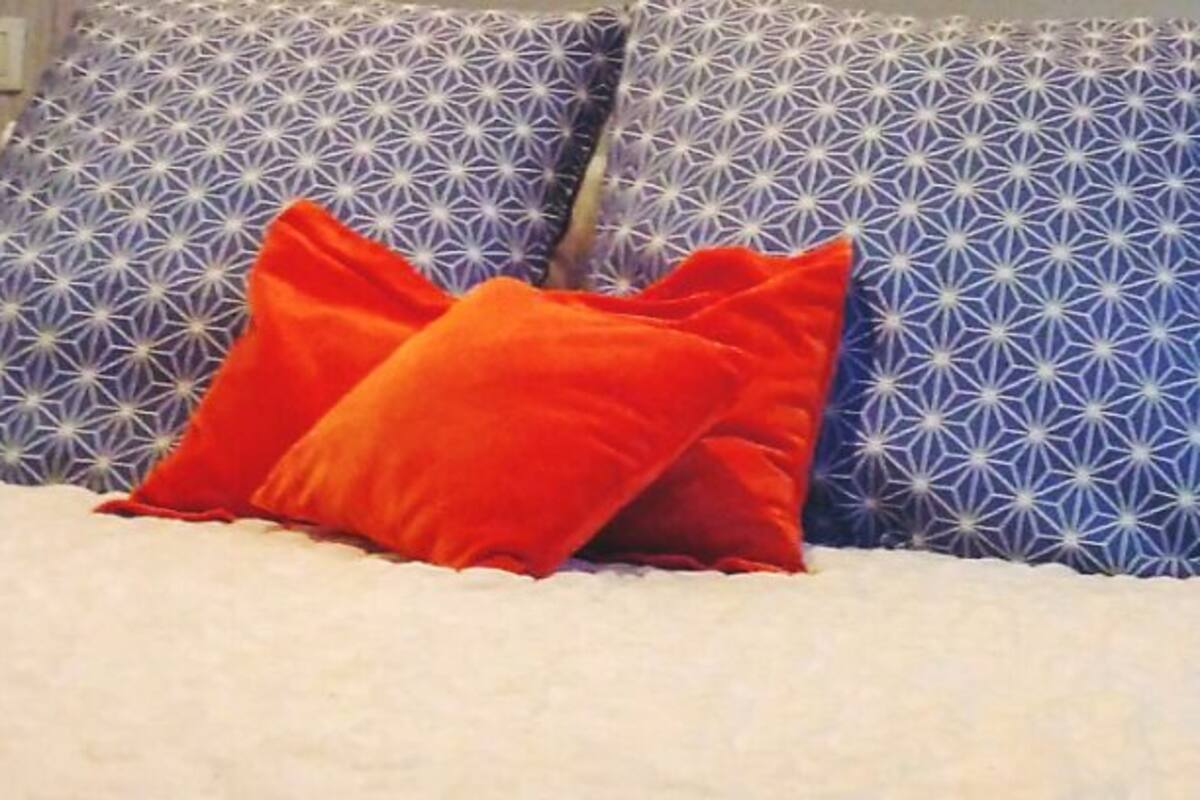 A bed with white bedding and two pillows, one orange and one blue with a geometric pattern.