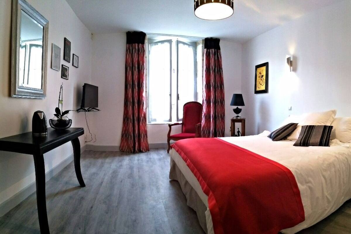 A hotel room with a bed, a desk, a chair, a lamp, and a window with curtains.