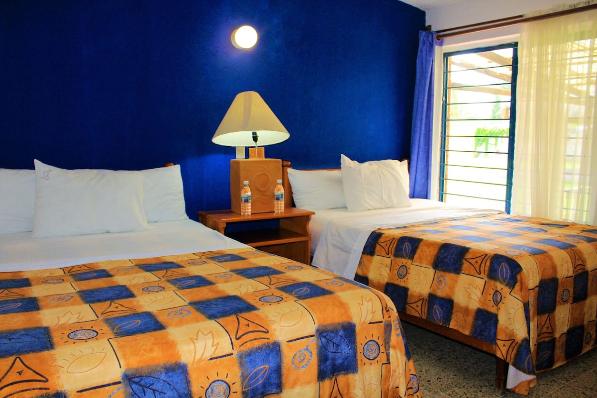 A hotel room with two beds, a nightstand with a lamp, and a window with curtains.