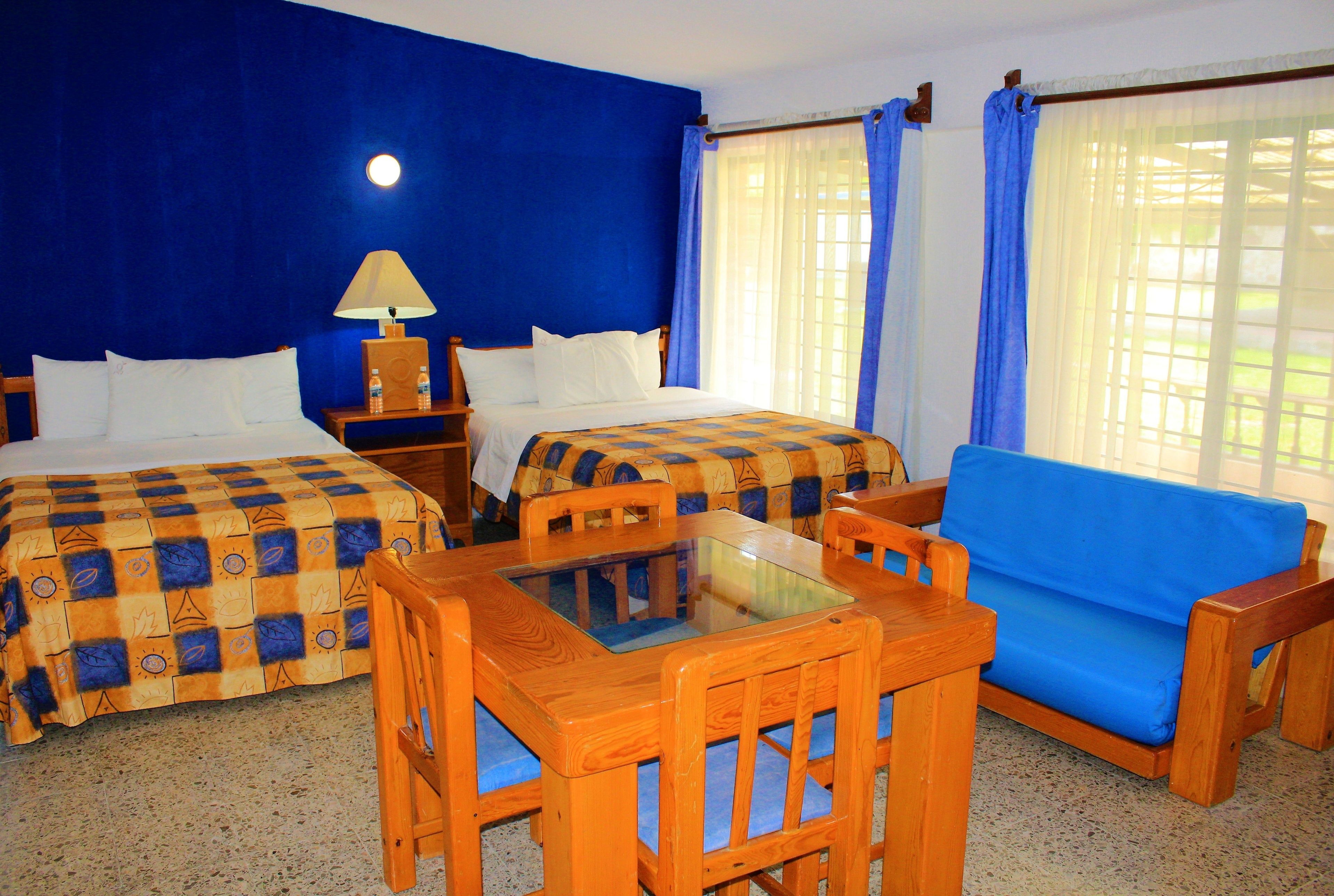 Habitación de hotel con dos camas, un sofá, una mesa de madera y una lámpara.