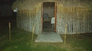 Una cabaña con techo de paja, una entrada sencilla y una cama pequeña visible en el interior.