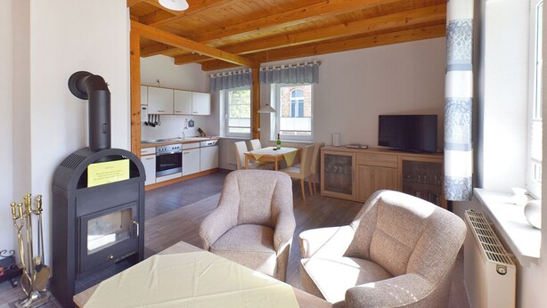 A cozy living room with a fireplace, two armchairs, a dining table, and a kitchen in the background. - Family-friendly terraced house with fireplace, WiFi, sauna, pets allowed (Ostseebad Prerow)