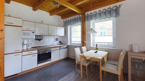 A compact kitchen with white cabinets, a microwave, stove, and a dining table with chairs. - Family-friendly terraced house with fireplace, WiFi, sauna, pets allowed (Ostseebad Prerow)