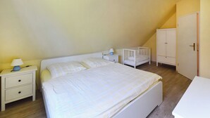 A bedroom with a bed, nightstand, crib, wardrobe, and a desk. - Family-friendly terraced house with fireplace, WiFi, sauna, pets allowed (Ostseebad Prerow)