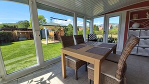 A conservatory with a dining table and chairs, large windows, and a view of a garden and buildings. - Holiday home "Zur Lehns" with garden (Darlingerode)
