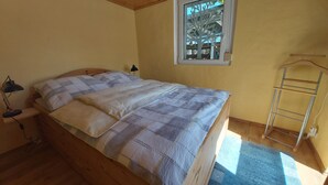 A bedroom with a wooden bed, a window with a tree view, a bedside lamp, and a wooden ladder. - Holiday home "Zur Lehns" with garden (Darlingerode)