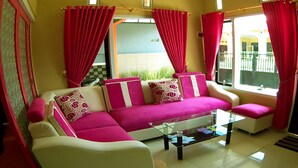 A living room with a sofa, two armchairs, a glass coffee table, and red curtains. - Kanalan Homestay (Banyuwangi)