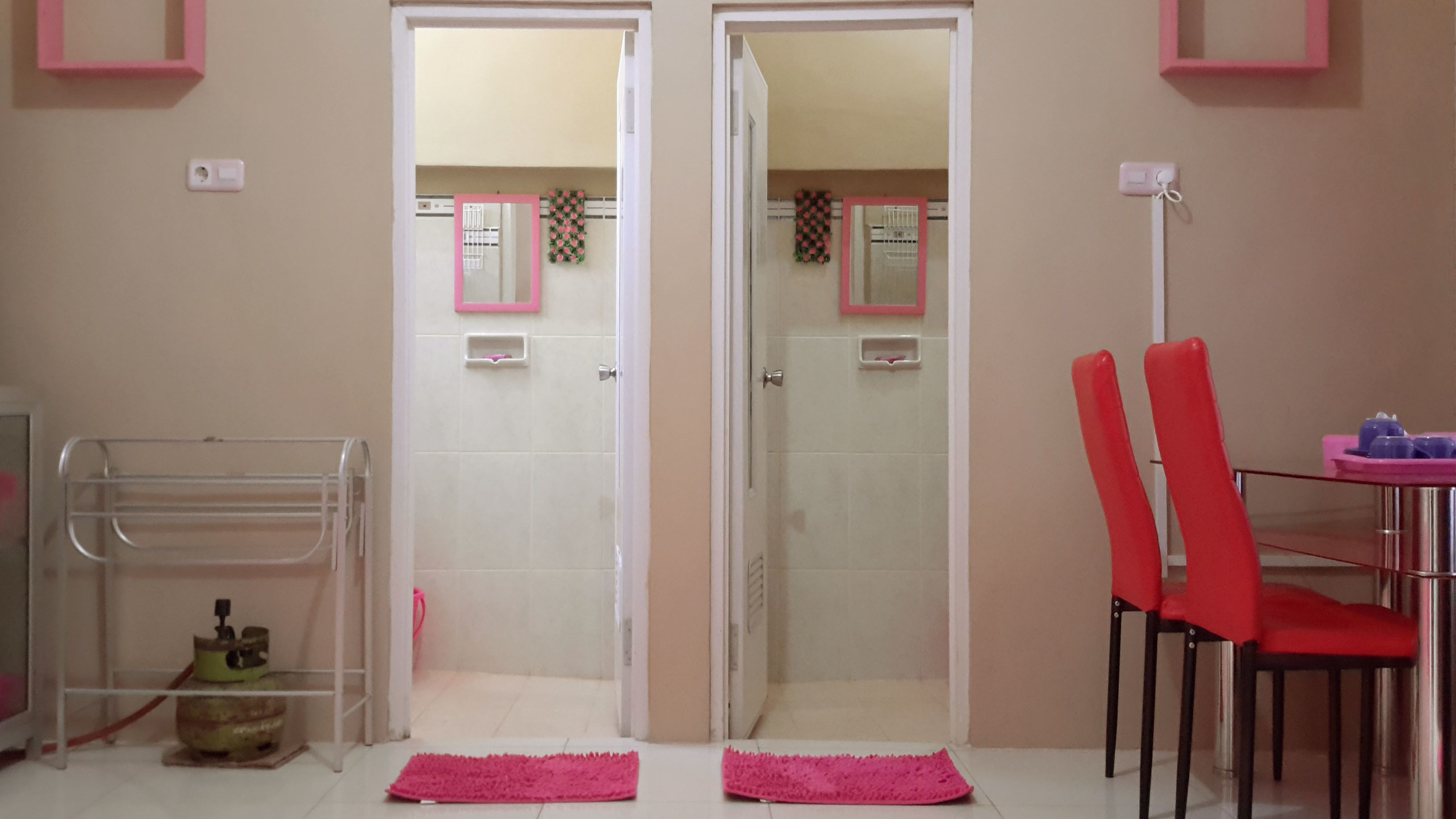 A bathroom with a shower, a toilet, and a sink. There are two red chairs and a table with a pink rug in front.
