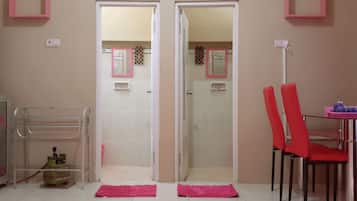 A bathroom with a shower, a toilet, and a sink. There are two red chairs and a table with a pink rug in front.