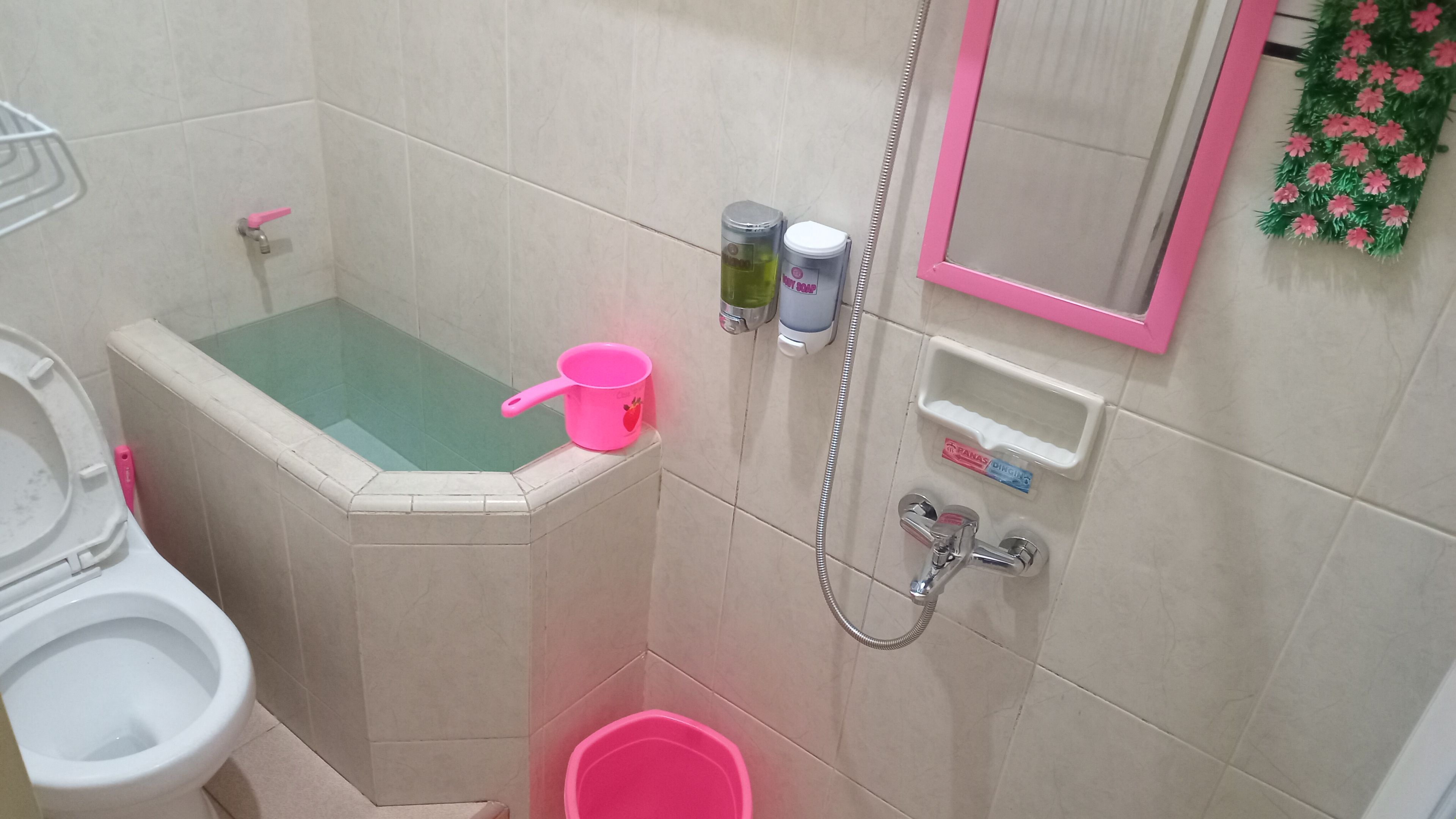 Une salle de bain avec une baignoire, des toilettes, une douche et un seau rose.