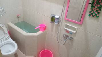 Une salle de bain avec une baignoire, des toilettes, une douche et un seau rose.