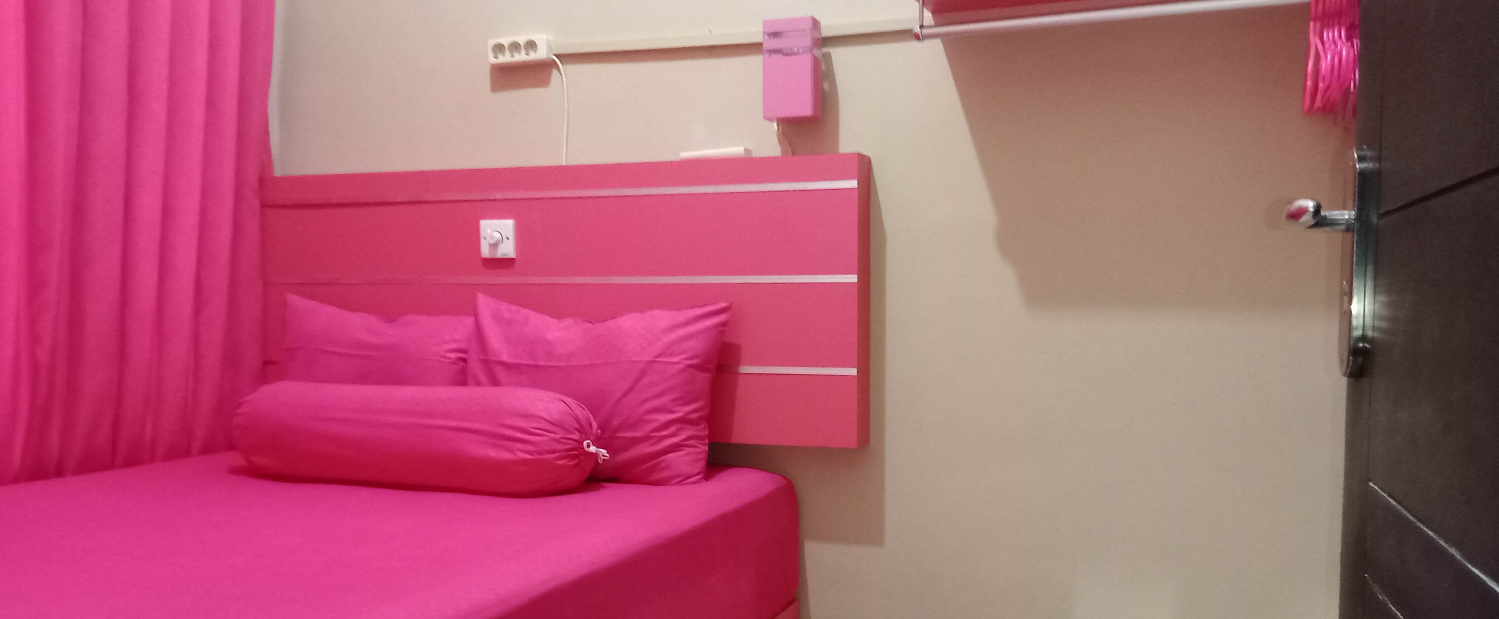 Un dormitori amb temàtica rosa que inclou un llit, una presa corrent a la paret i una porta.