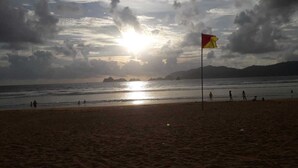 A beach with a flag, ocean, and distant mountains. - Kanalan Homestay (Banyuwangi)