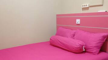 Een kamer met een roze bed, een wit paneel en een beigekleurige muur.