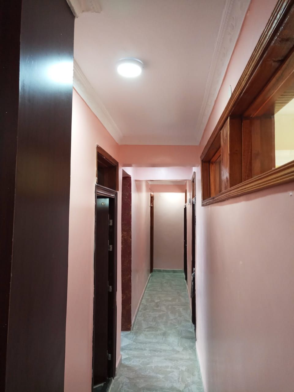 Un pasillo estrecho con suelo de baldosas, puertas de madera y una lámpara en el techo.