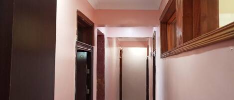 Un pasillo estrecho con suelo de baldosas, puertas de madera y una lámpara en el techo.