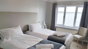 A hotel room with two beds, a chair, and a window with a view of the water.