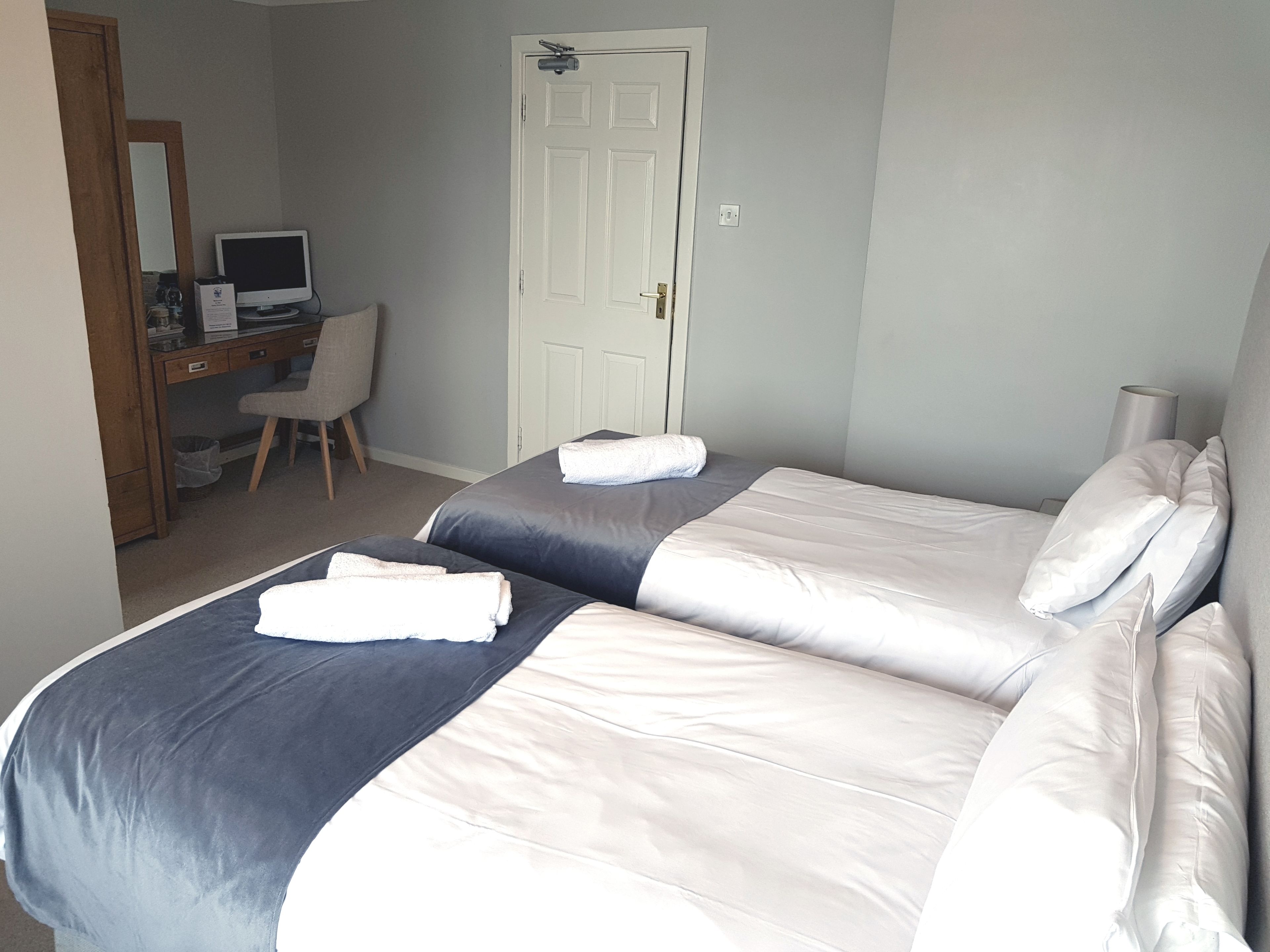 A hotel room with two beds, a desk with a computer, a chair, and a door.