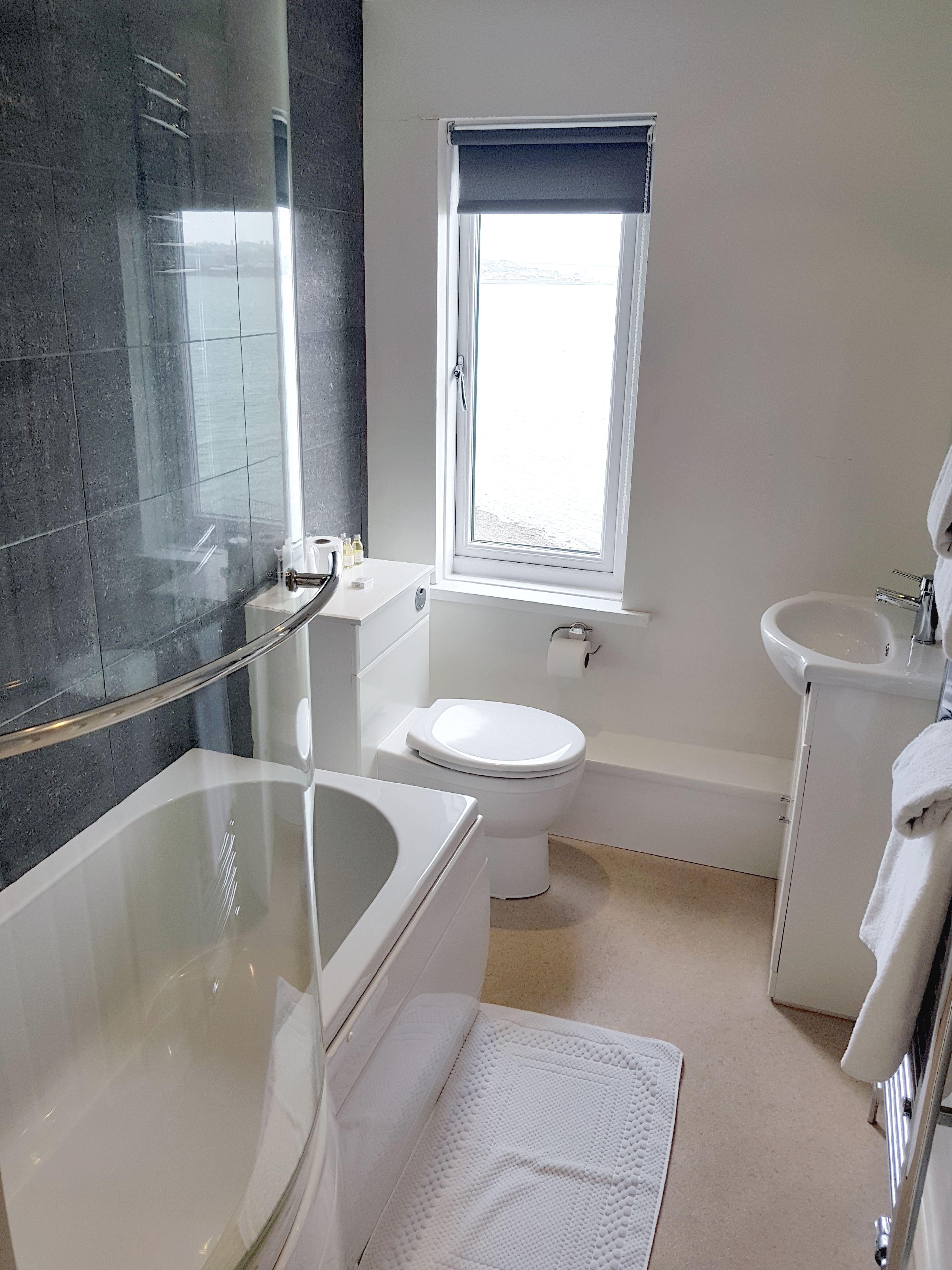 Un baño moderno con cabina de ducha de vidrio, bañera, inodoro y ventana que proporciona luz natural.