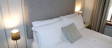 A neatly made bed with white linens and a grey headboard, two bedside lamps, and a striped pillow.