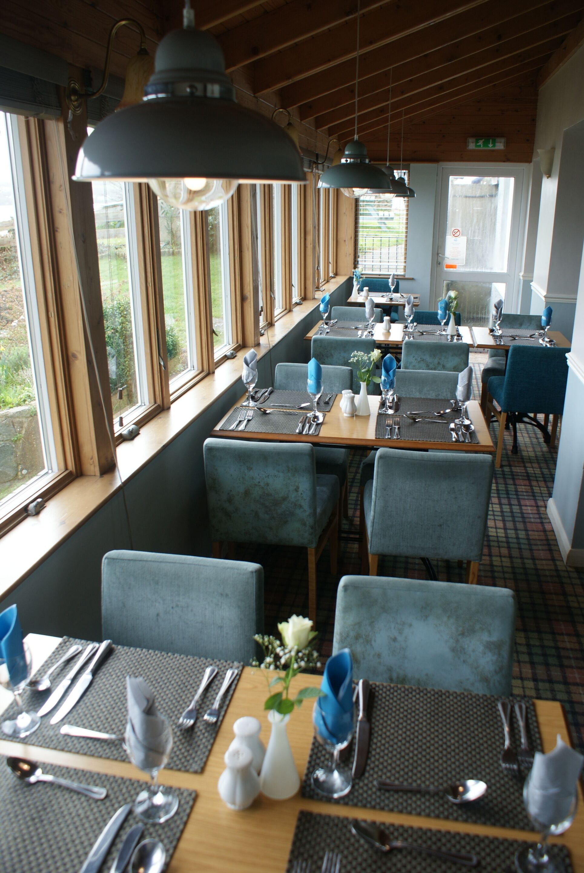 A restaurant with tables set for dining, large windows, and blue chairs.