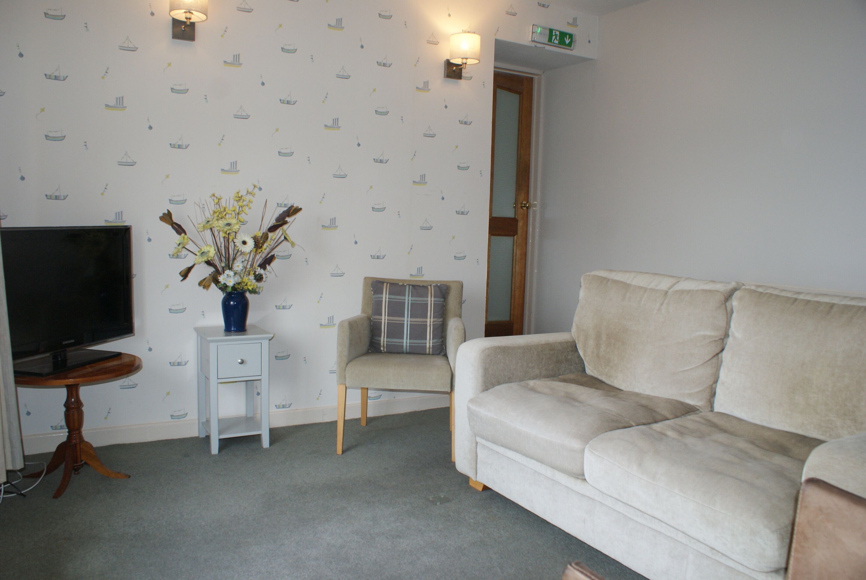 A living room with a beige sofa, a small white table with a vase, a television, and a chair.