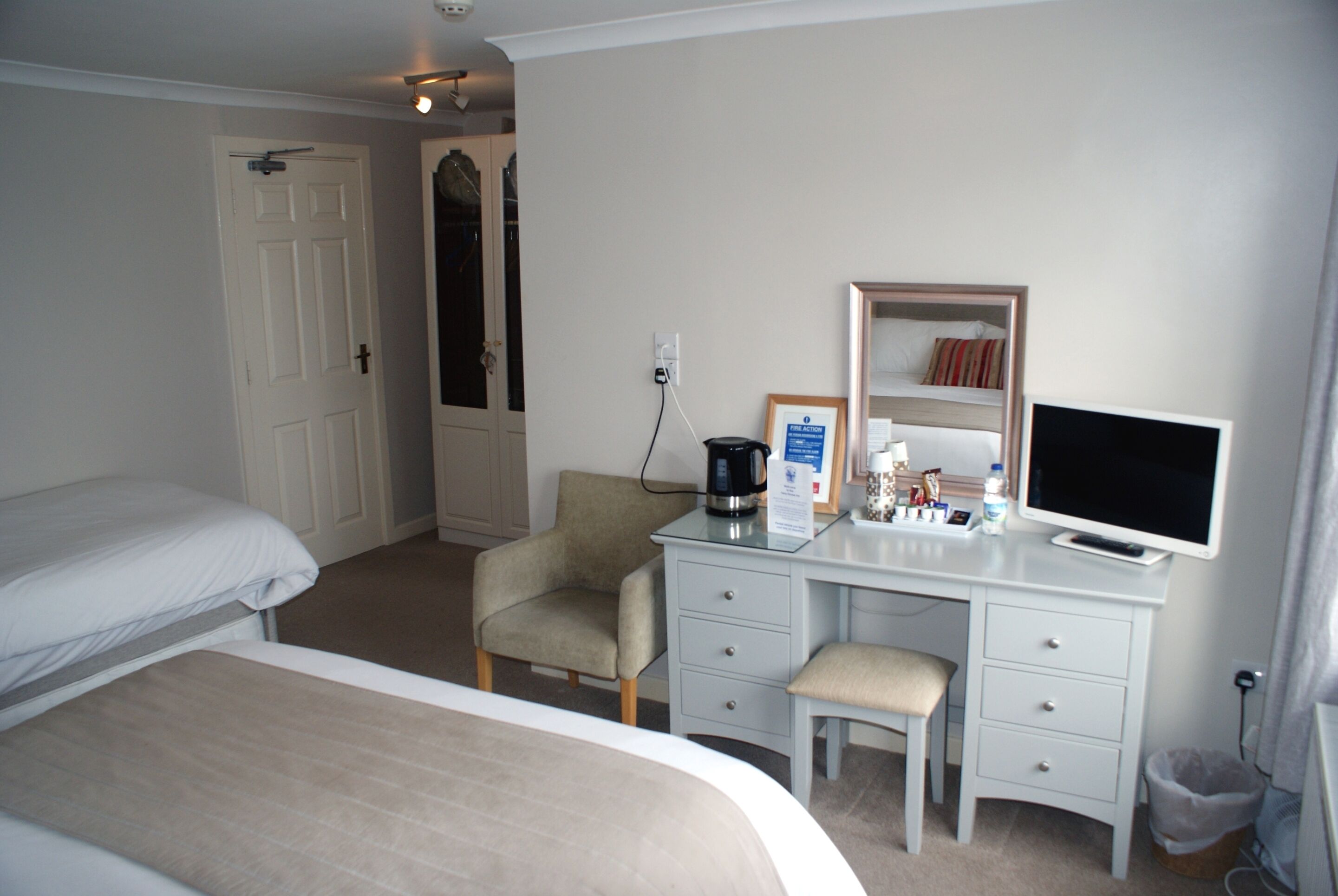 A hotel room with two beds, a desk with a computer, a chair, and a small trash bin.