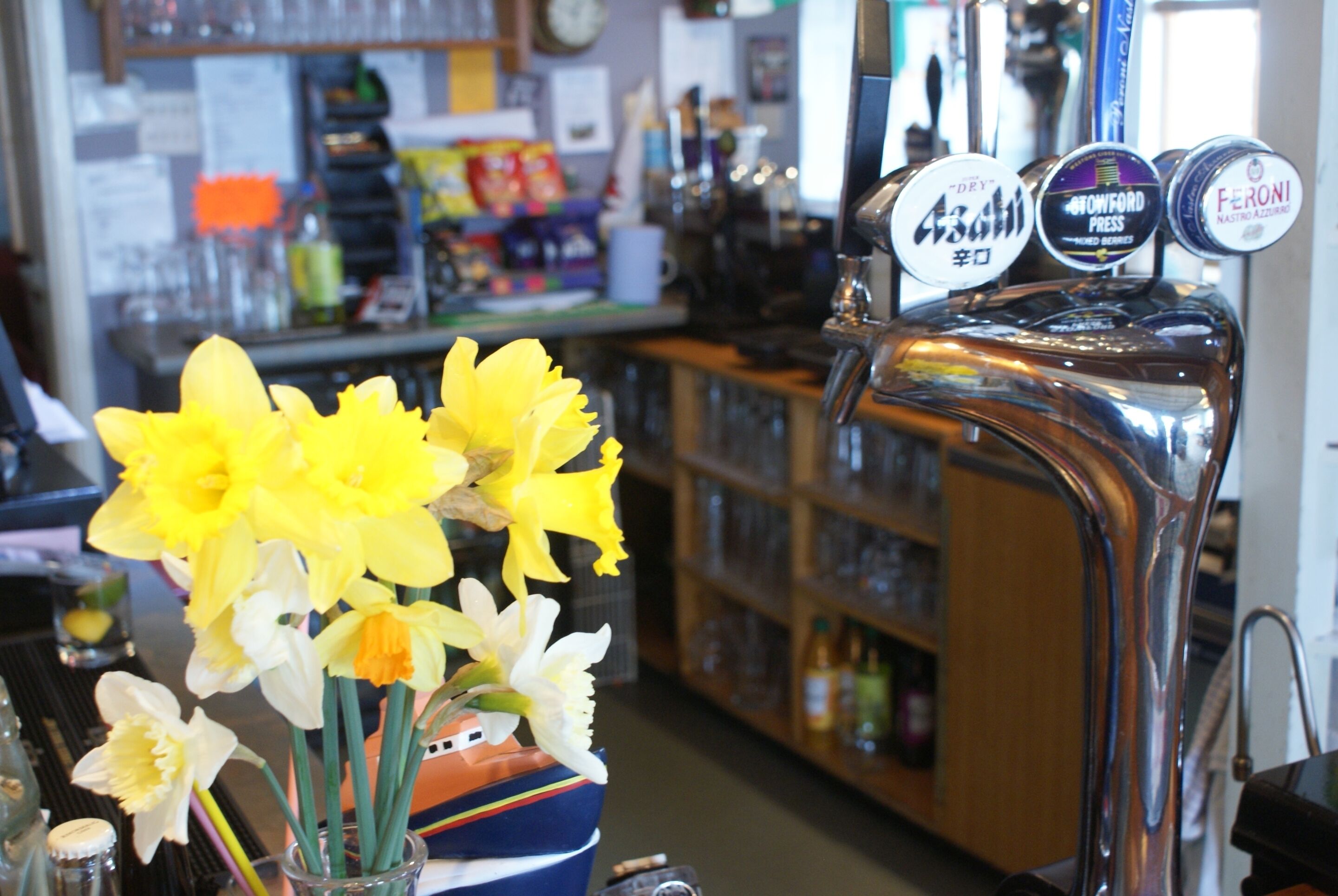 A bar area with a beer tap and a vase of yellow and white flowers.