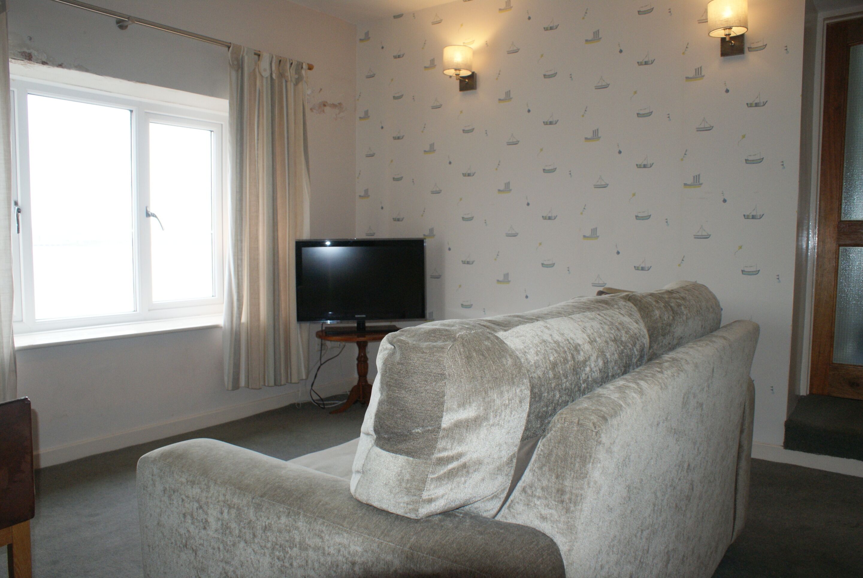A living room with a large window, a flat-screen TV, and a patterned wallpaper.