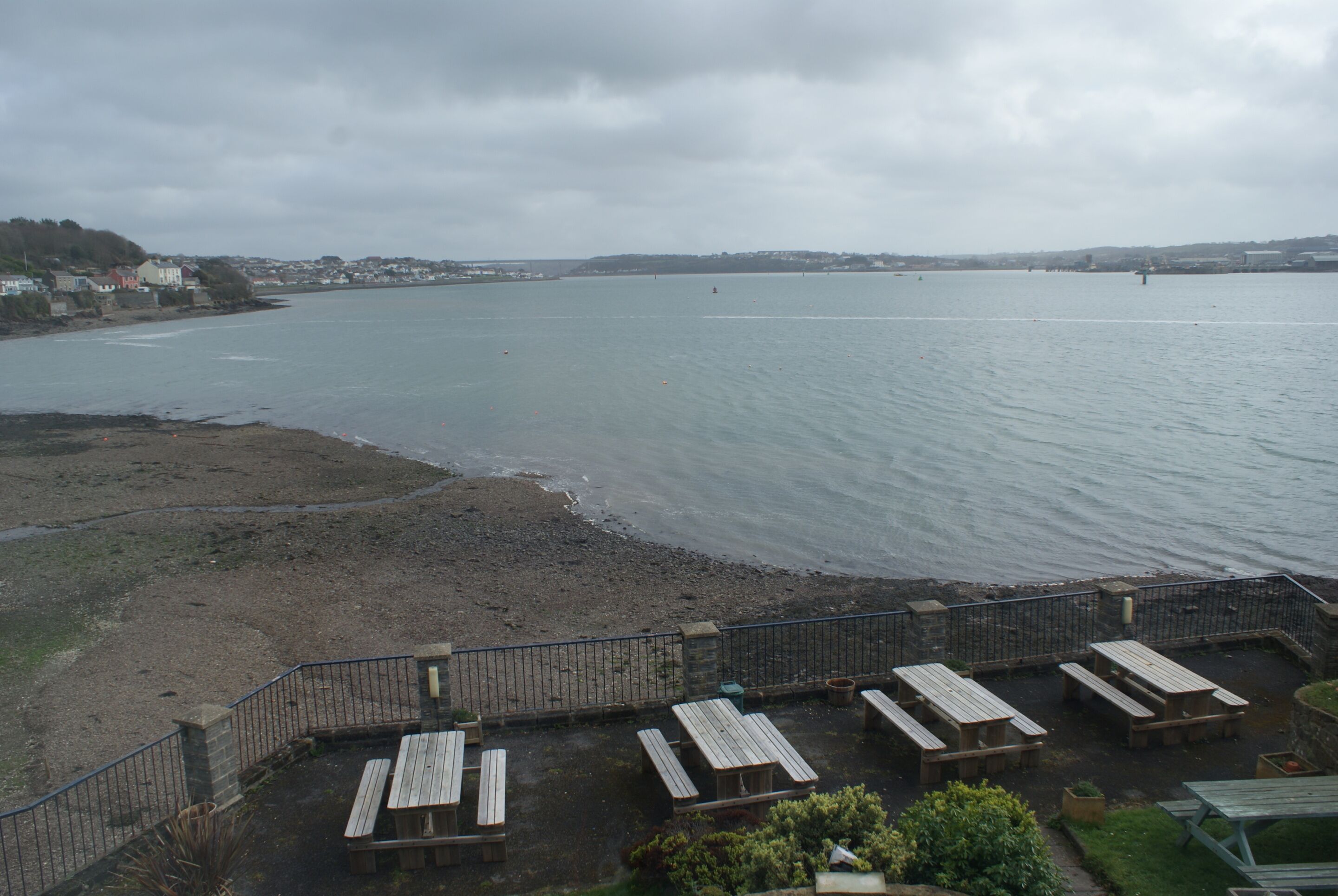 A coastal view with a wooden deck and picnic tables overlooking the sea.