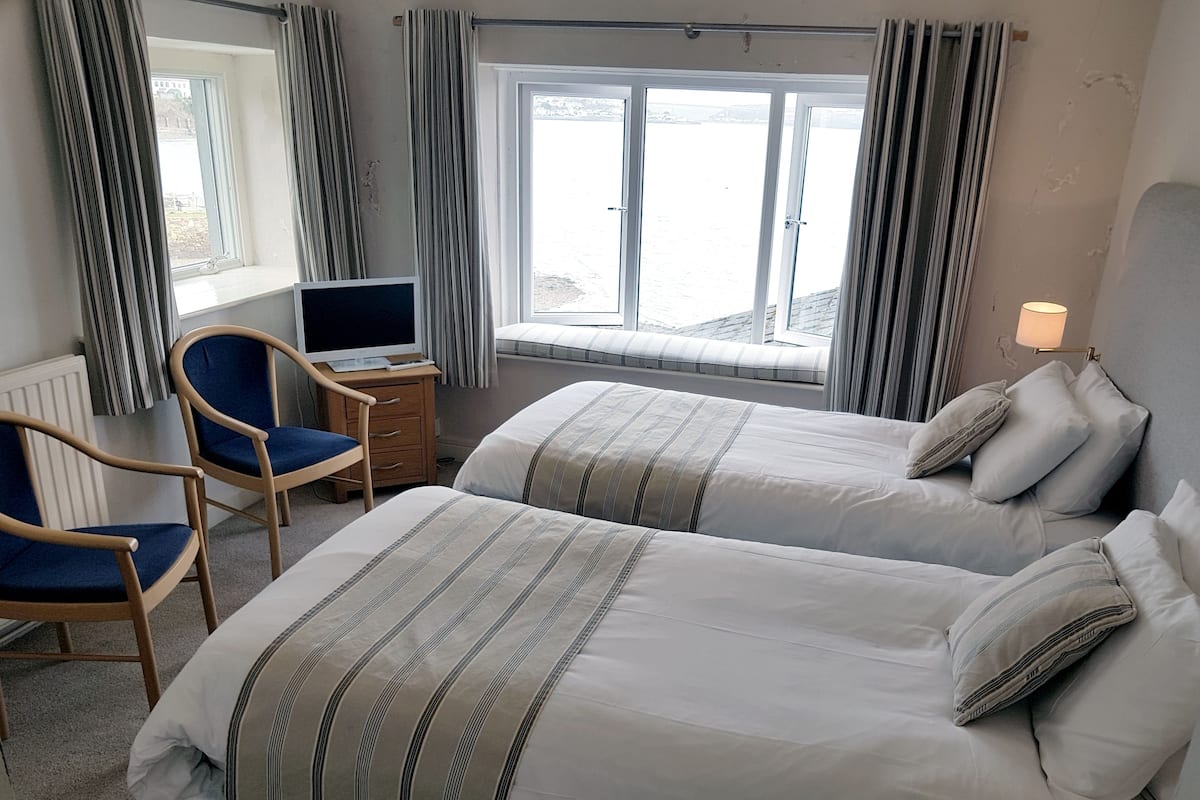 Une chambre d’hôtel avec deux lits, un bureau avec un ordinateur, une chaise et une fenêtre avec des rideaux.