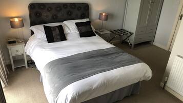 A neatly made bed with white and grey bedding, two bedside lamps, a small bedside table with a radio, and a radiator.