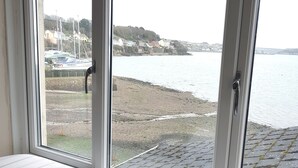 A window seat with a striped cushion, overlooking a harbor with boats and buildings.
