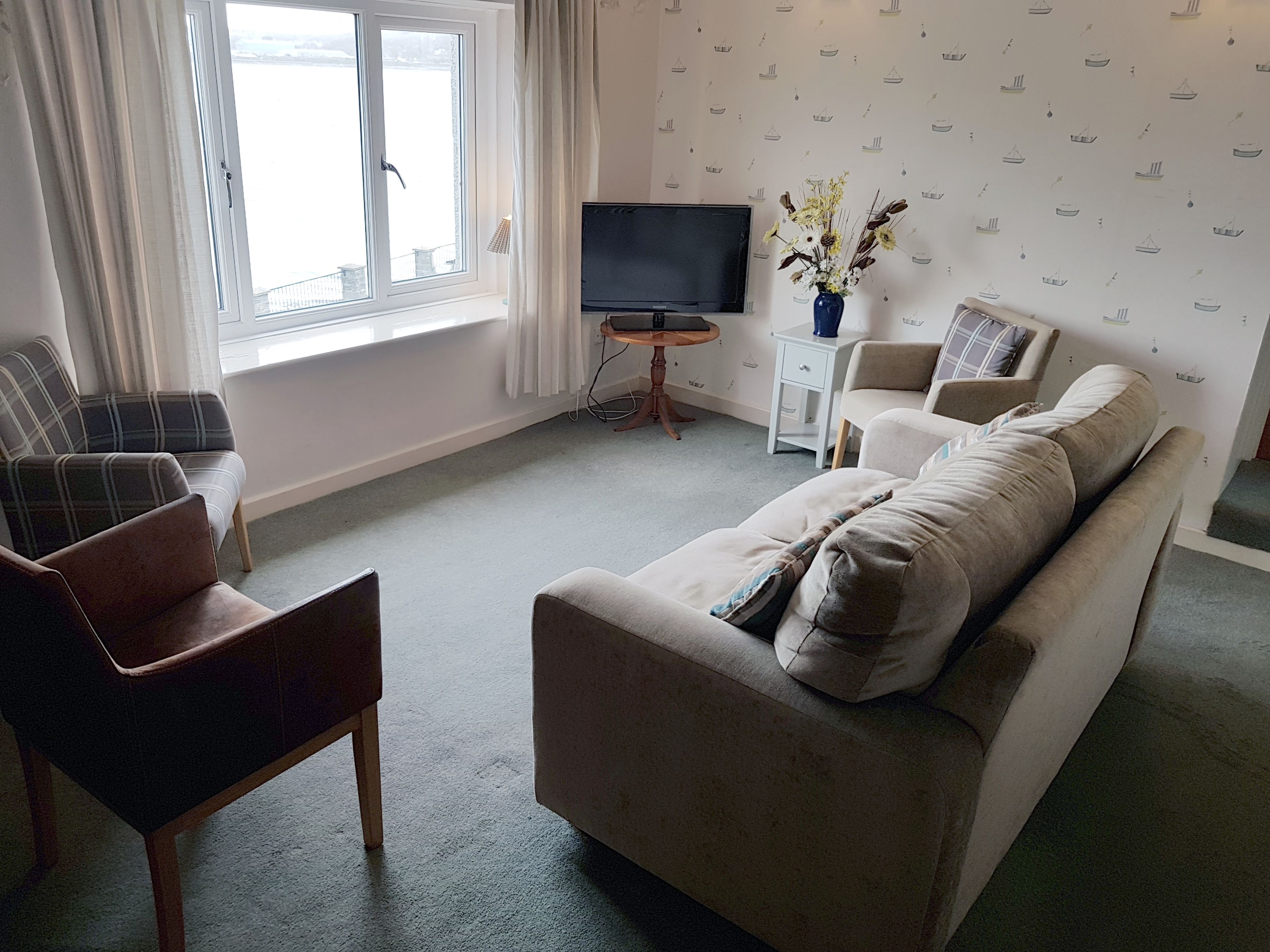 Una sala de estar con sofá, sillas, televisor y ventana.