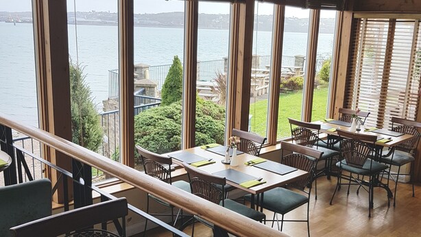 A restaurant with a view of a body of water, wooden interior, and multiple tables and chairs.