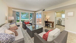 A spacious living area with a large window, a dining table, and a kitchen in the background. - Unit #203 Sand Cay Beach Resort Gulf Front (Longboat Key)