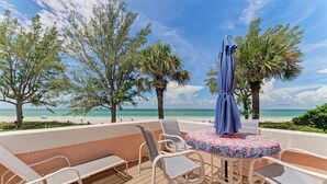 A deck with lounge chairs and a table, overlooking a beach with palm trees and the ocean. - Unit #203 Sand Cay Beach Resort Gulf Front (Longboat Key)