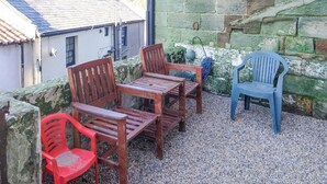 A patio with wooden furniture and a blue plastic chair, surrounded by stone walls and a gravel floor. - 3 bedroom accommodation in Staithes, near Saltburn-by-the-Sea (Staithes, near Saltburn-by-the-Sea)