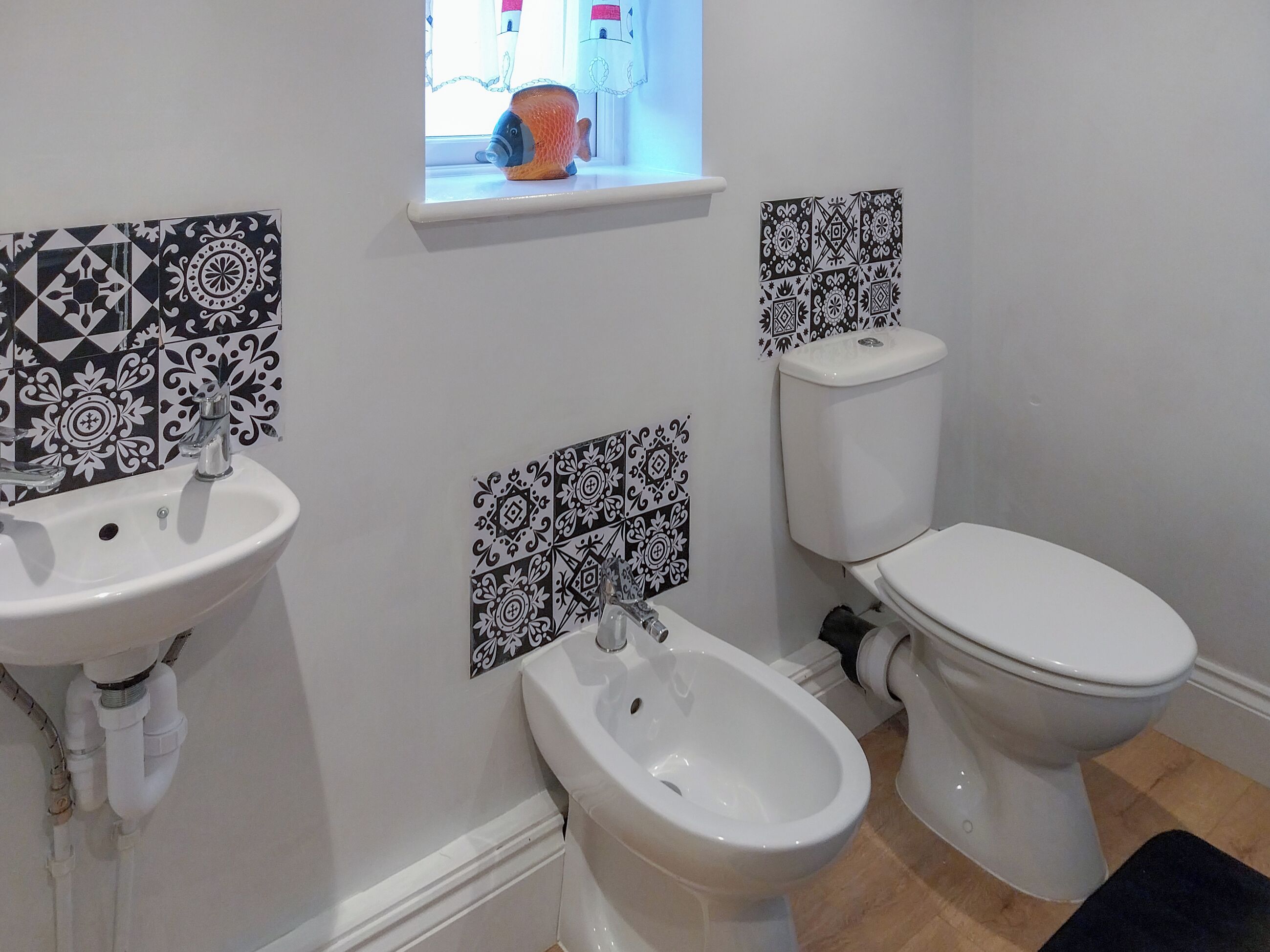 A bathroom with a sink, bidet, toilet, and decorative black and white tiles.