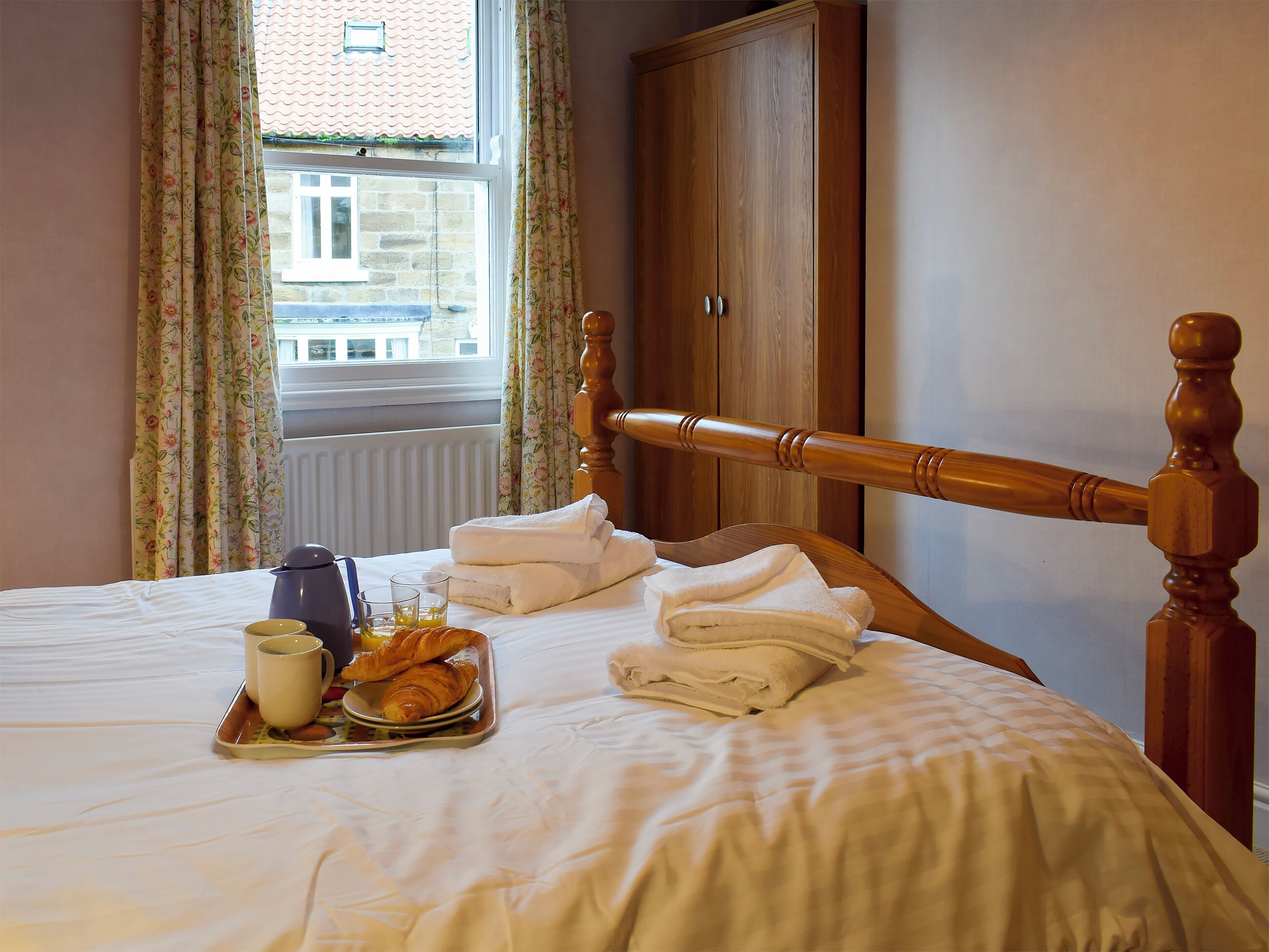 Een opgemaakt bed met handdoeken, een dienblad met croissants en een kopje, wat een ontbijtarrangement doet vermoeden.