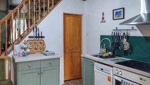 A kitchen with a wooden staircase, a sink with hanging utensils, a stove, and a wooden door. - 3 bedroom accommodation in Staithes, near Saltburn-by-the-Sea (Staithes, near Saltburn-by-the-Sea)