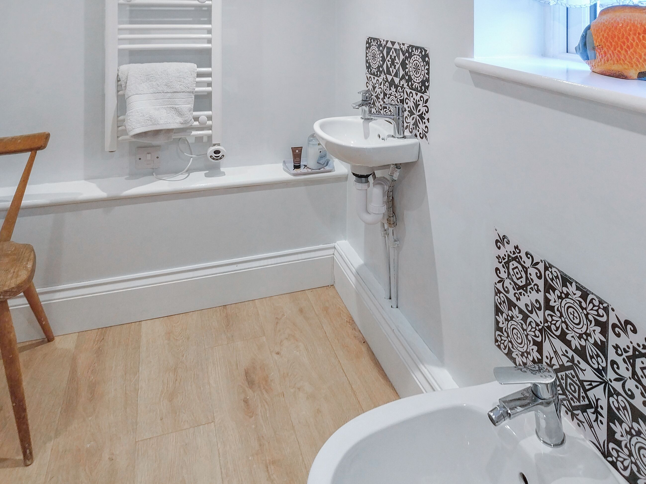 A bathroom with a bathtub, a sink, and a toilet. There is a wooden chair and a towel rack.