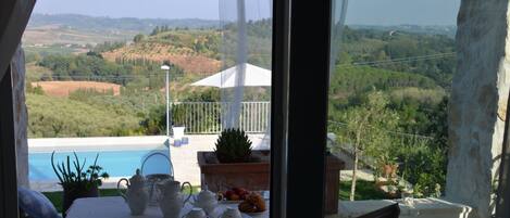 A balcony with a table set for tea, a view of a swimming pool, and a lush landscape.