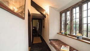 A narrow hallway with a wooden bench, a small table with a book and a mug, and a window with a view of trees. - The Old Priory Cottage (Dunster, near Minehead)