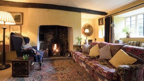 A cozy living room with a fireplace, a patterned sofa, and a traditional lamp. - The Old Priory Cottage (Dunster, near Minehead)
