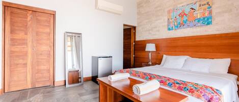 Une chambre d’hôtel avec un lit en bois, un banc, une petite table, une poubelle et une armoire.