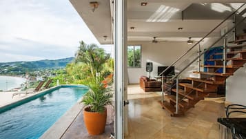 A modern interior with a pool, a staircase, and a view of the beach.